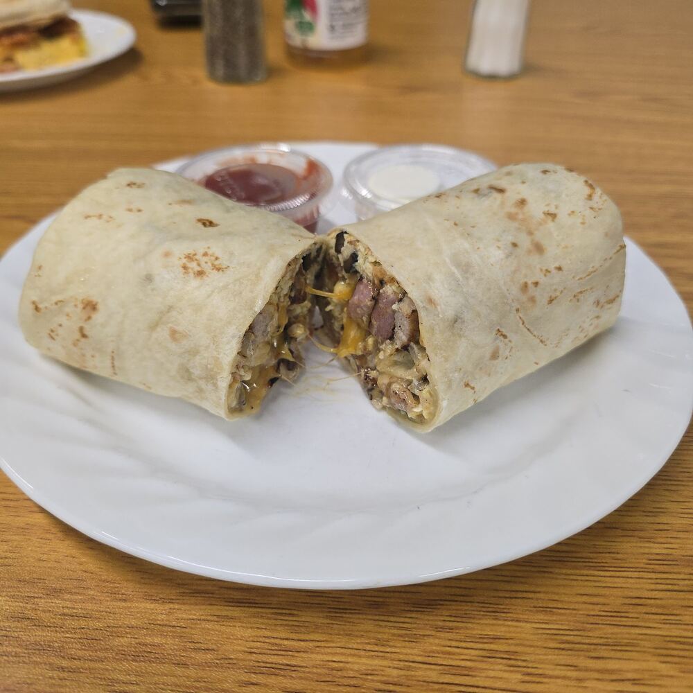 Breakfast burrito in a toasted flour tortilla, cut in half to show scrambled egg, sausage, melted cheddar, potato and mushroom, with cups of salsa and sour cream.