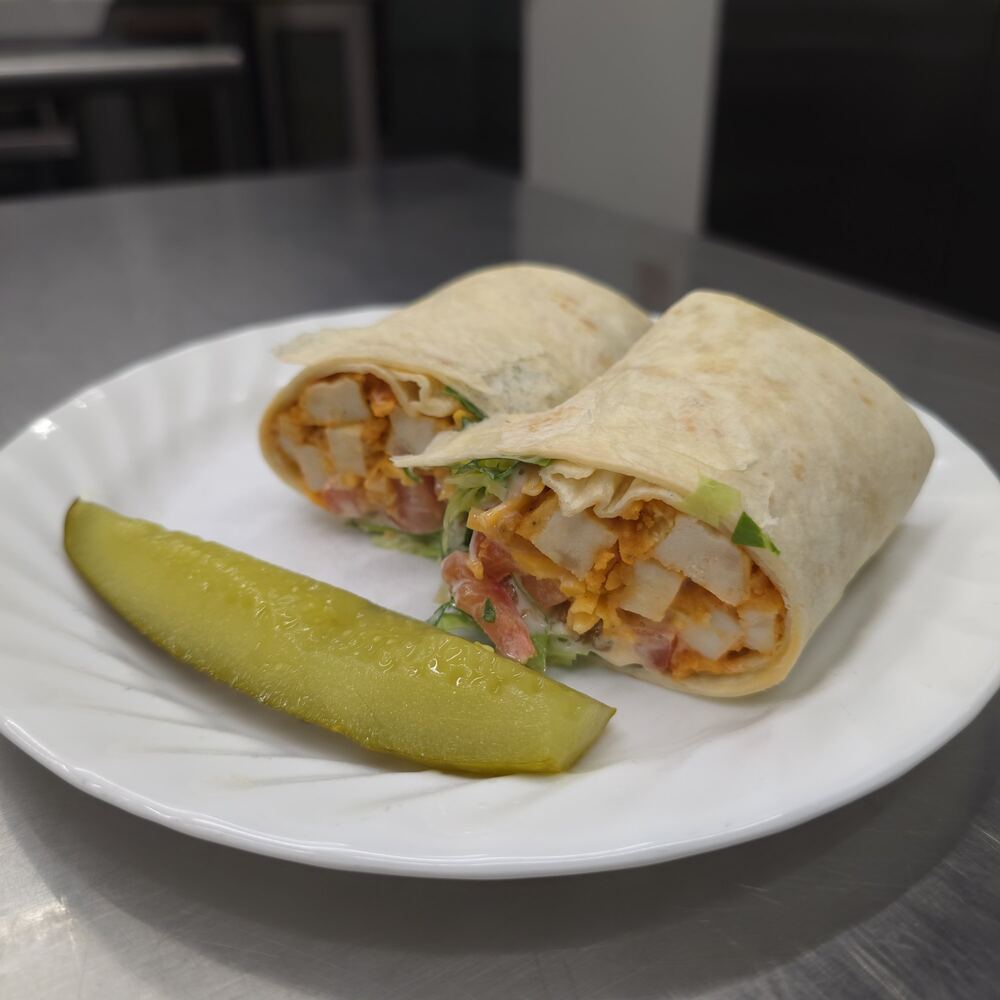 Buffalo chicken wrap in a flour tortilla, cut in half to show buffalo chicken, tomato, cheese and lettuce, with a pickle spear.