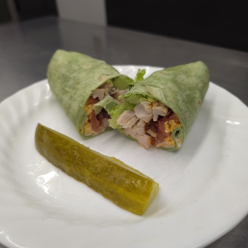 Chicken bacon wrap in a spinach tortilla, cut in half to show chicken, bacon, cheese and lettuce, with a pickle spear.
