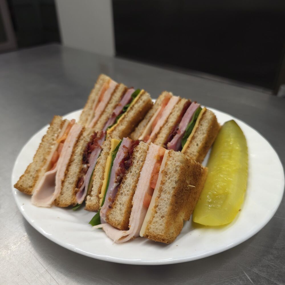 Triple-decker clubhouse sandwich on white toast, cut into quarters to show turkey, ham, bacon, cheese, lettuce and tomato, with a pickle spear.