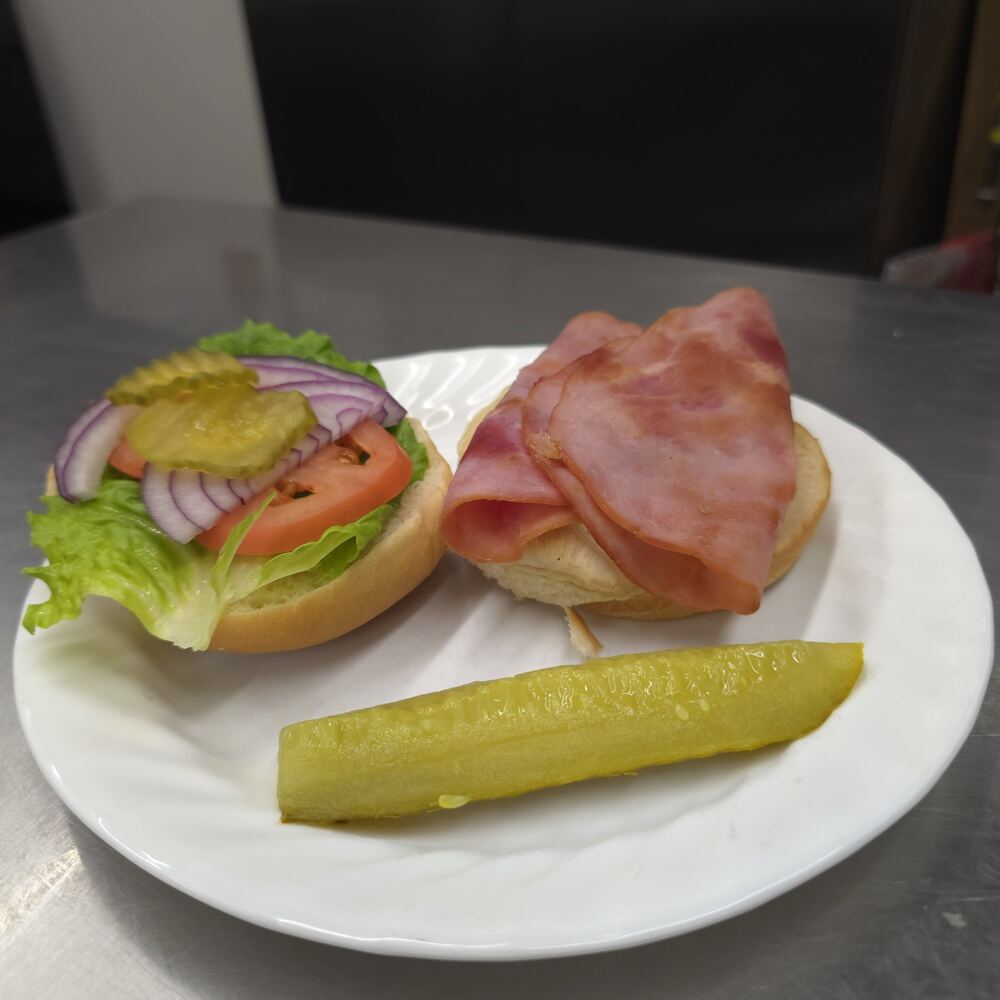 Cordon bleu chicken sandwich served open-faced: chicken under folded ham on a bun, the top bun with lettuce, tomato, red onion and pickles, and a pickle spear.