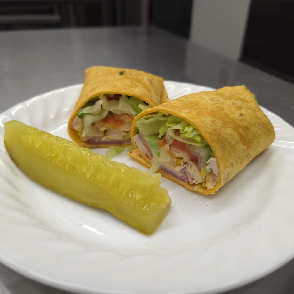 Cordon bleu wrap in a tomato-basil tortilla, cut in half to show ham, chicken, cheese, lettuce and tomato, with a pickle spear.