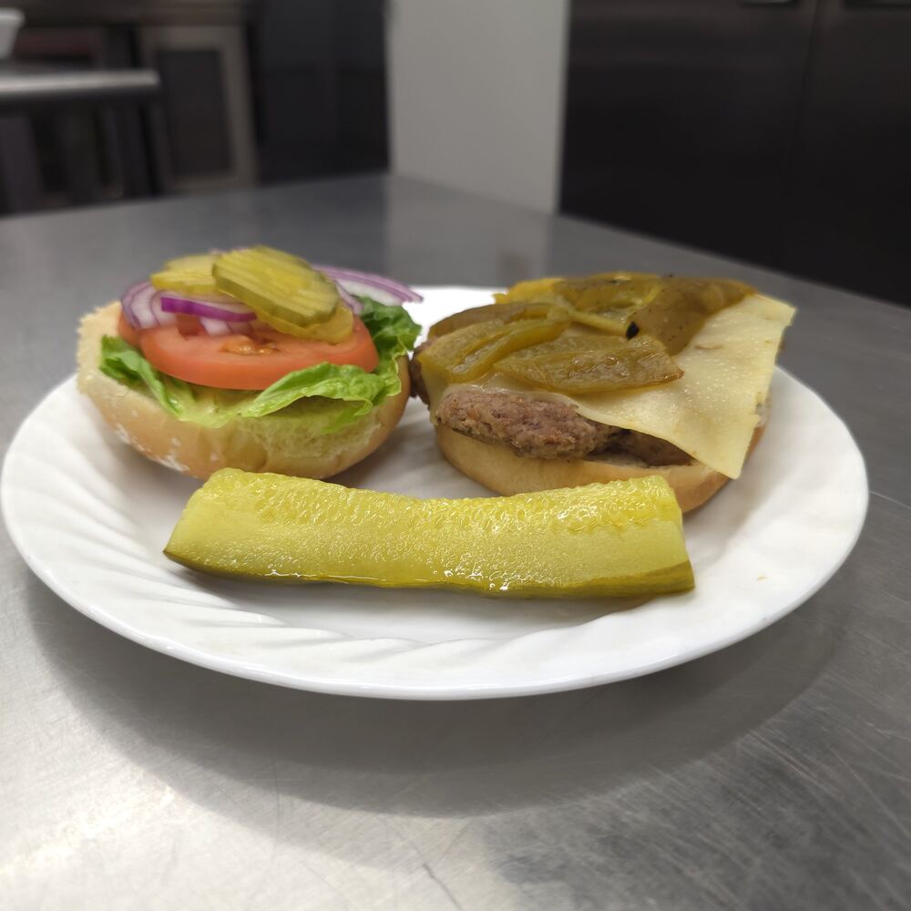 Navajo burger served open-faced: a beef patty topped with green chiles and pepper jack cheese, the top bun with lettuce, tomato, red onion and pickles, and a pickle spear.
