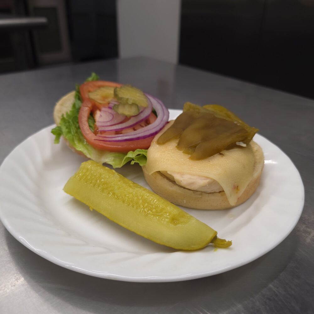Navajo chicken sandwich served open-faced: chicken topped with pepper jack cheese and green chiles, the top bun with lettuce, tomato, red onion and pickles, and a pickle spear.