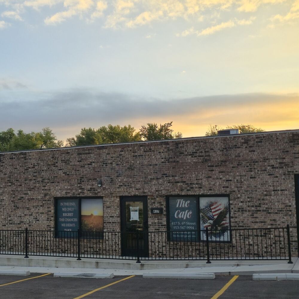 The Café's brick storefront at 417 South 6th St at sunset: the front door between two windows, one with the cafe's name, address and phone number, behind a black railing.
